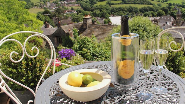 Une table avec une bouteille de Prosecco, deux verres et un saladier de fruits.