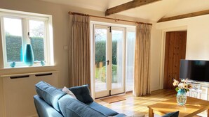 Una sala de estar con sofá, una mesa de centro, televisor y ventana con cortinas.