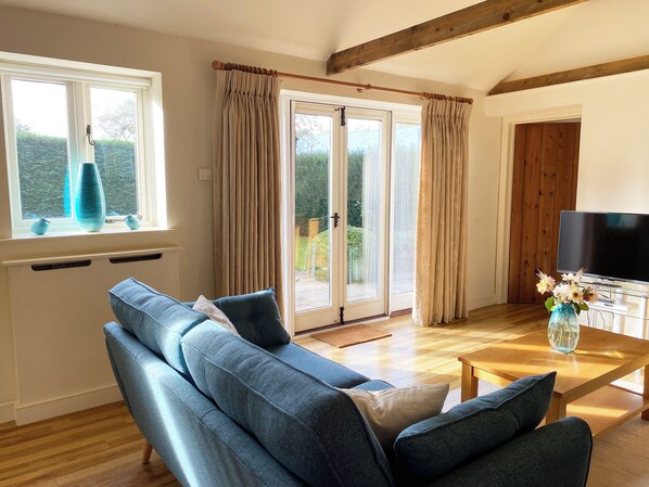 A living room with a sofa, a coffee table, a TV, and a window with curtains. - 2 bedroom accommodation in Occold, near Eye (Occold, near Eye)