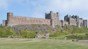 Eine große Burg mit mehreren Türmen und einer befestigten Mauer, gelegen auf einem grasbewachsen Hügel unter einem wolkenlosen Himmel.