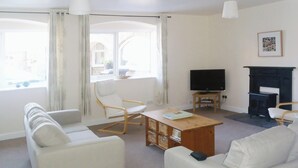 Ein Wohnzimmer mit einer Couch, Sesseln, einem Couchtisch, einem Fernseher und einem Kamin.