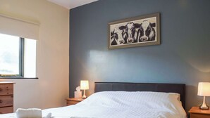 A neatly made bed with white linens and towels, a dark headboard, and a framed picture of cows on the wall.