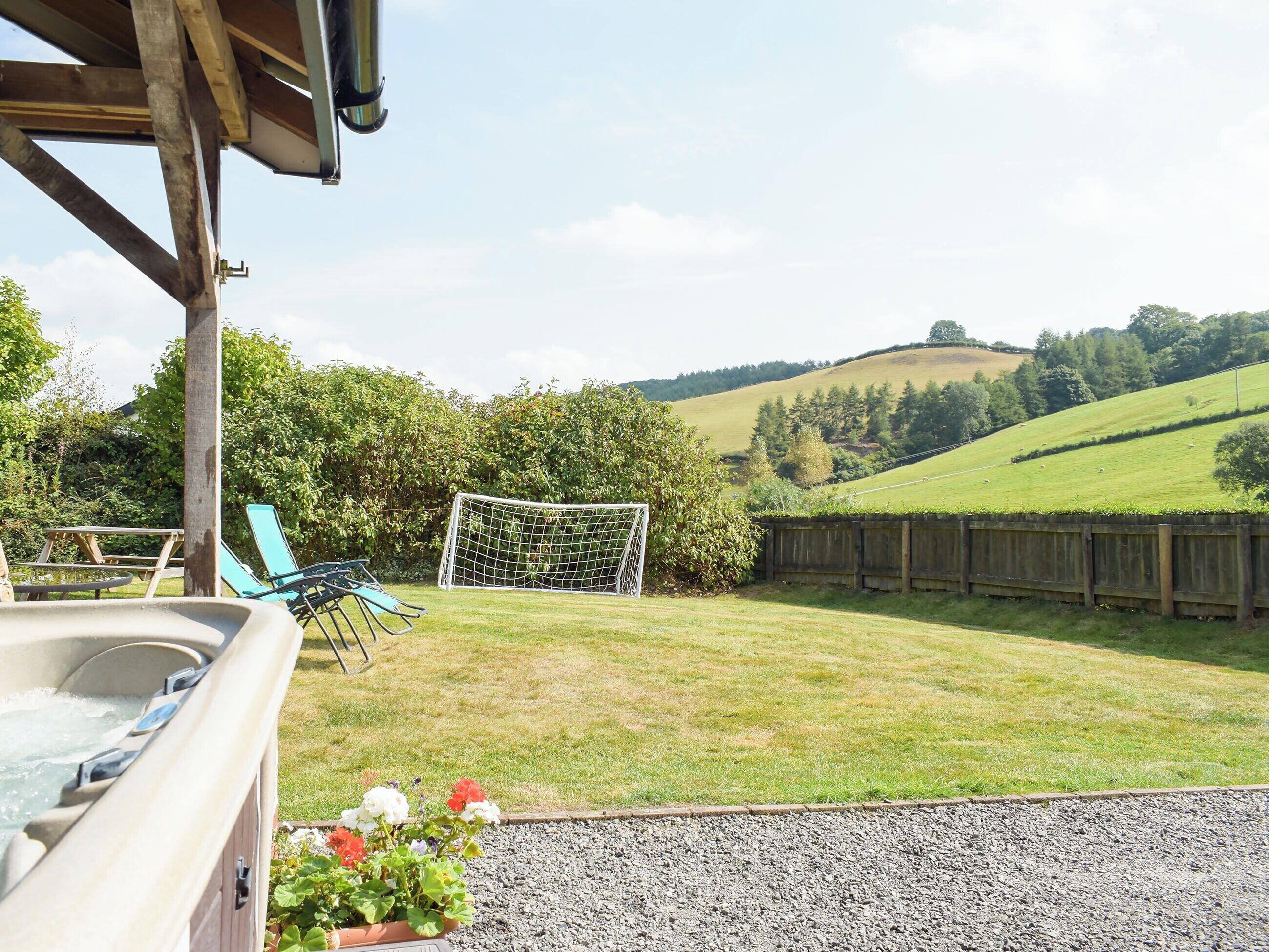Un bain à remous avec une terrasse en bois, une pelouse, une clôture en bois et une vue panoramique sur les collines et les arbres.