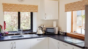 A kitchen with white cabinets, a microwave, a kettle, and a window with a view of greenery.