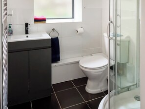 A bathroom with a white sink, dark cabinets, a toilet, and a glass shower enclosure. - Heyope Cottage (Heyope, near Knighton)