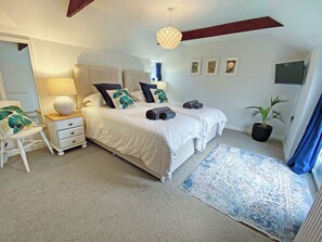 Une chambre avec deux lits, une table de chevet, une lampe, une plante en pot et un téléviseur fixé au mur.