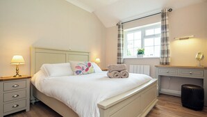 Ein Schlafzimmer mit Bett, Nachttischen, einem Schreibtisch und einem Fenster mit Vorhängen.