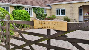 Ein hölzernes Schild mit der Aufschrift "LUKINGTON STABLES", vor einem Gebäude mit einem Ziegeldach und Steinmauern.