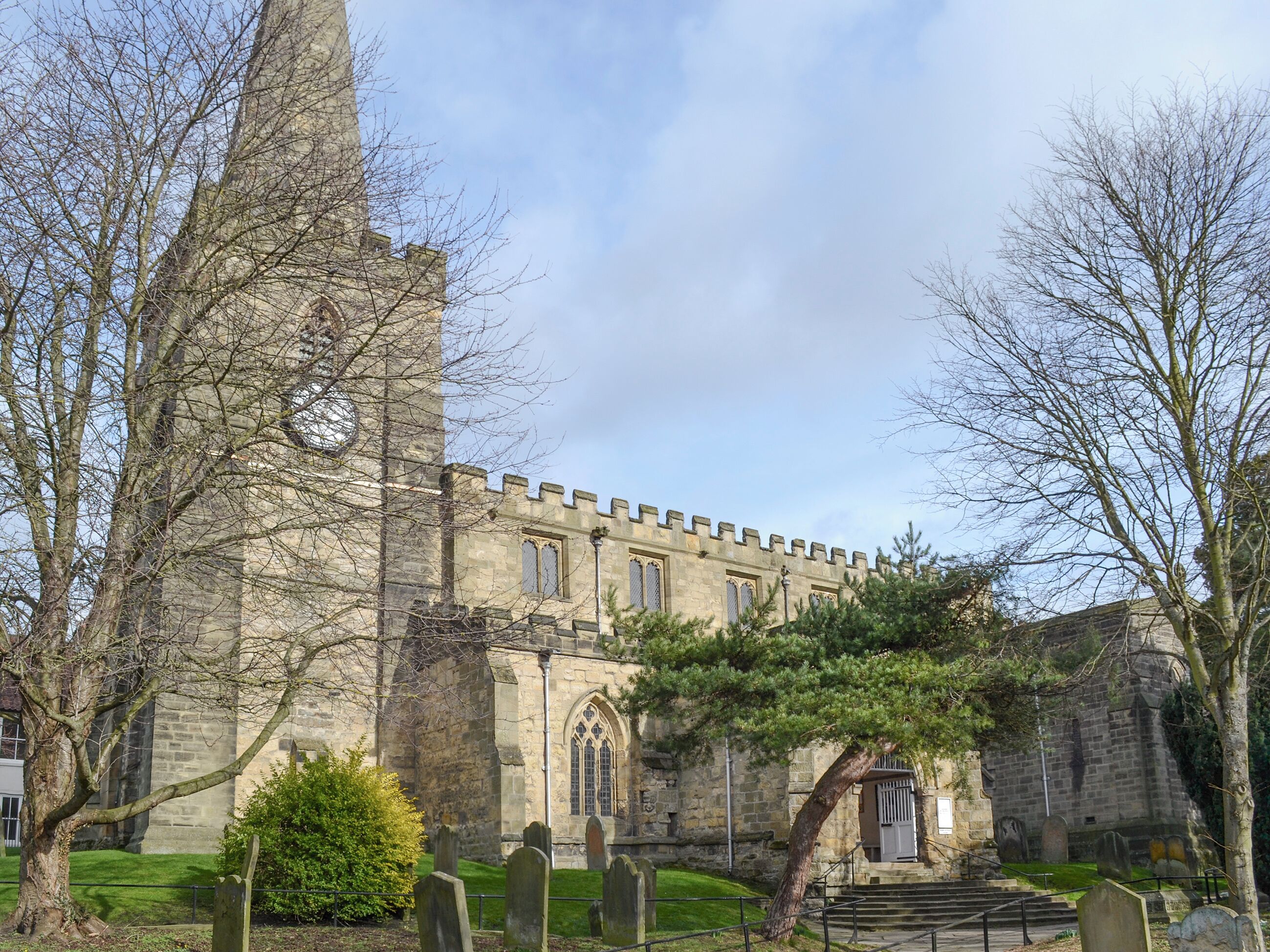 A historic stone building with a tall tower, a cemetery with headstones, and a well-maintained lawn.