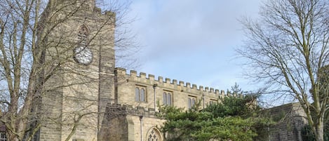 A historic stone building with a tall tower, a cemetery with headstones, and a well-maintained lawn.