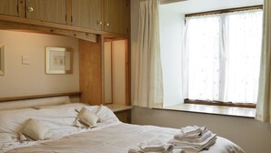 Una cama bien hecha con almohadas y toallas dobladas, cabecera de madera y una ventana con cortinas.