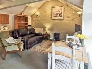 A cozy living room with a fireplace, a sofa, a dining table with chairs, a bookshelf, and a stone wall.