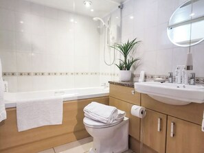 A modern bathroom with a bathtub, toilet, sink, and a potted plant.