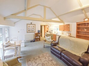 A spacious living area with a leather sofa, a dining table, and a kitchen in the background.