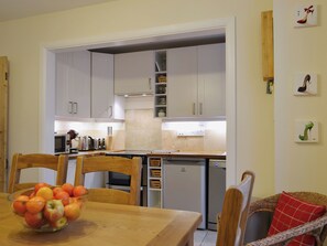 A kitchen with white cabinets, a dining table with a fruit bowl, and a wicker chair.