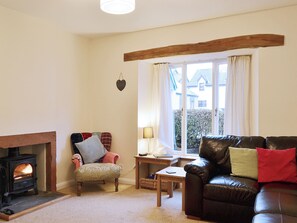 A cozy living room with a fireplace, a leather sofa, a wooden table, and a window with curtains.