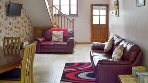 A living room with a wooden staircase, a dining area with a table and chairs, and a sofa with a patterned throw.
