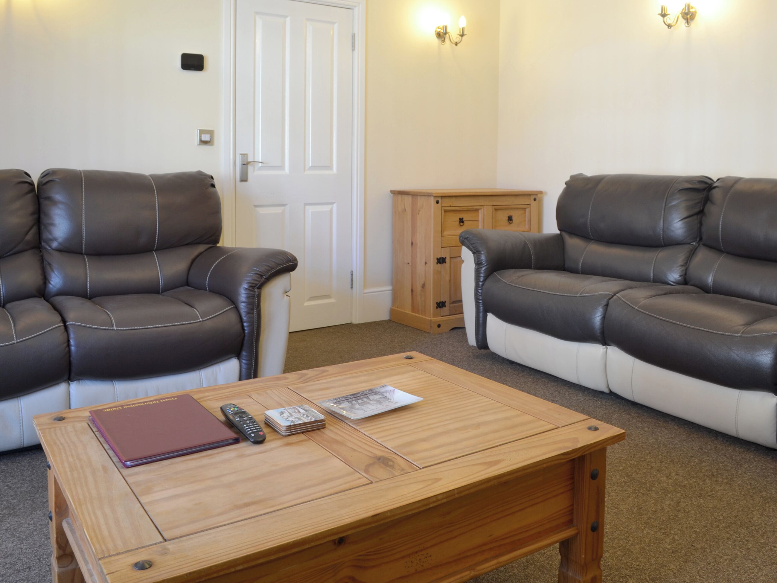 A living room with two leather sofas, a wooden coffee table, a remote control, a magazine, and a small wooden cabinet.