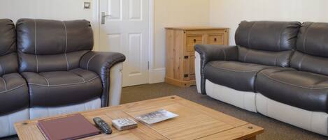 A living room with two leather sofas, a wooden coffee table, a remote control, a magazine, and a small wooden cabinet.