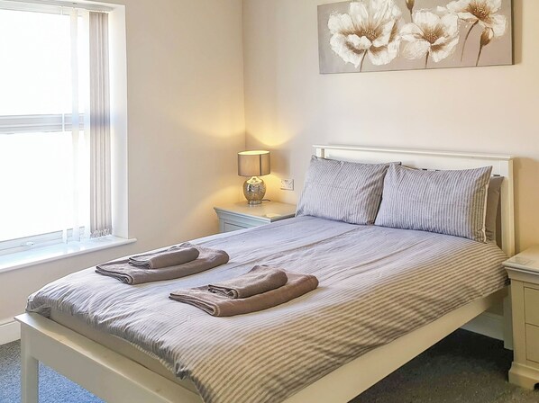A neatly made bed with striped bedding, a bedside lamp, and a wall-mounted artwork of flowers.