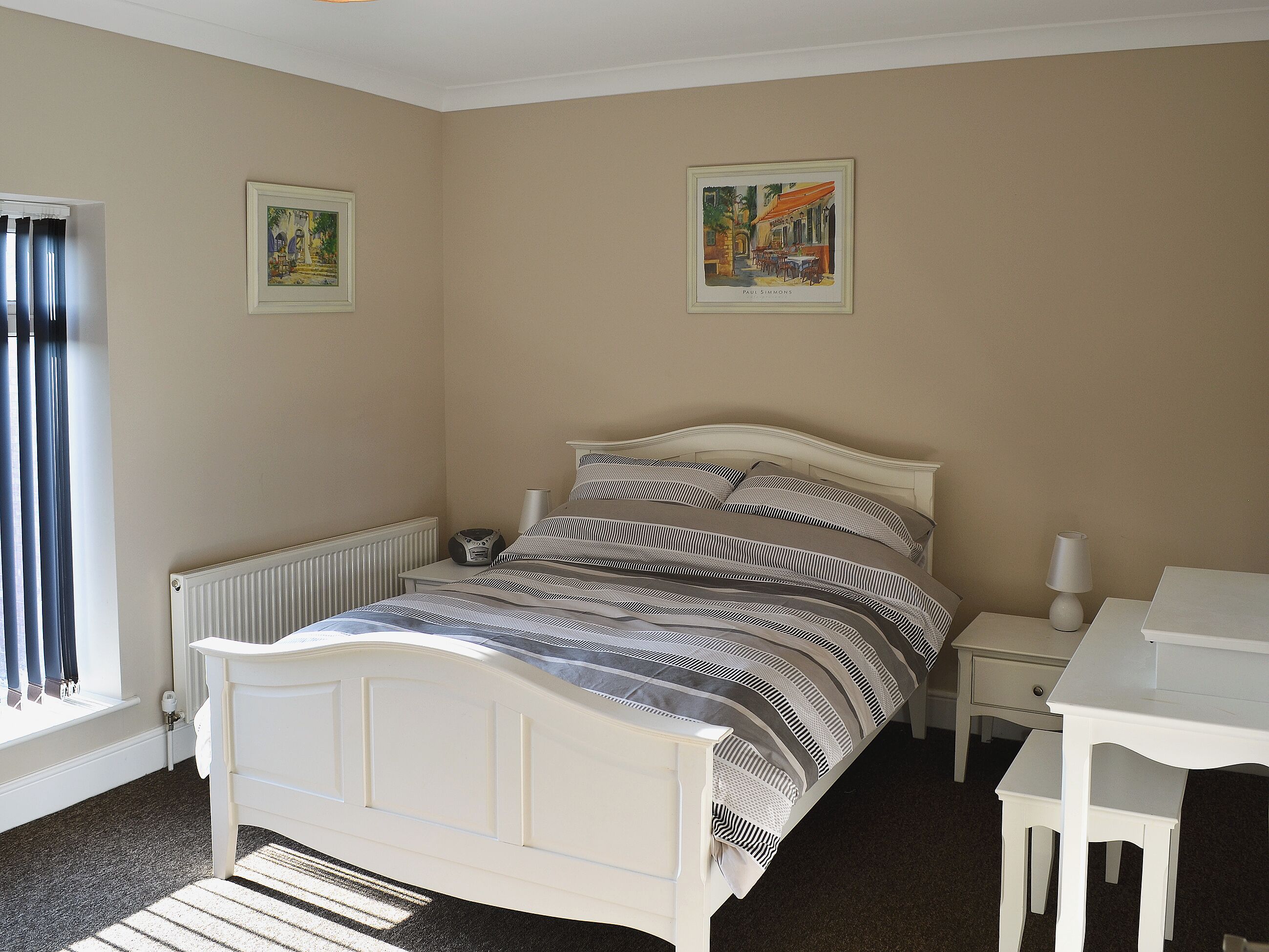 Une chambre à coucher avec un lit, des tables de chevet, un radiateur et deux tableaux encadrés accrochés au mur.