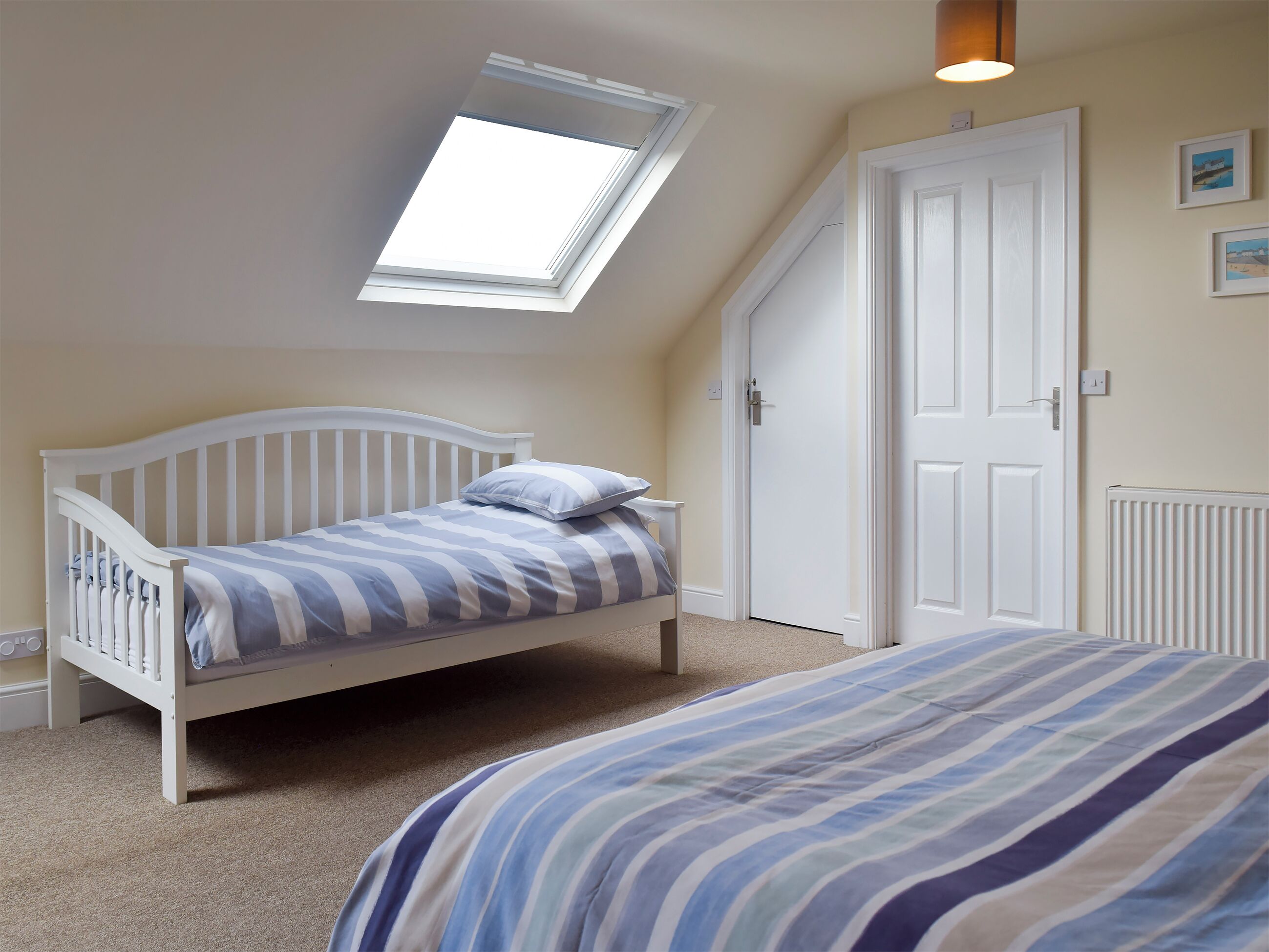 A bedroom with a sloped ceiling, a skylight, a white door, and a bed with striped bedding.