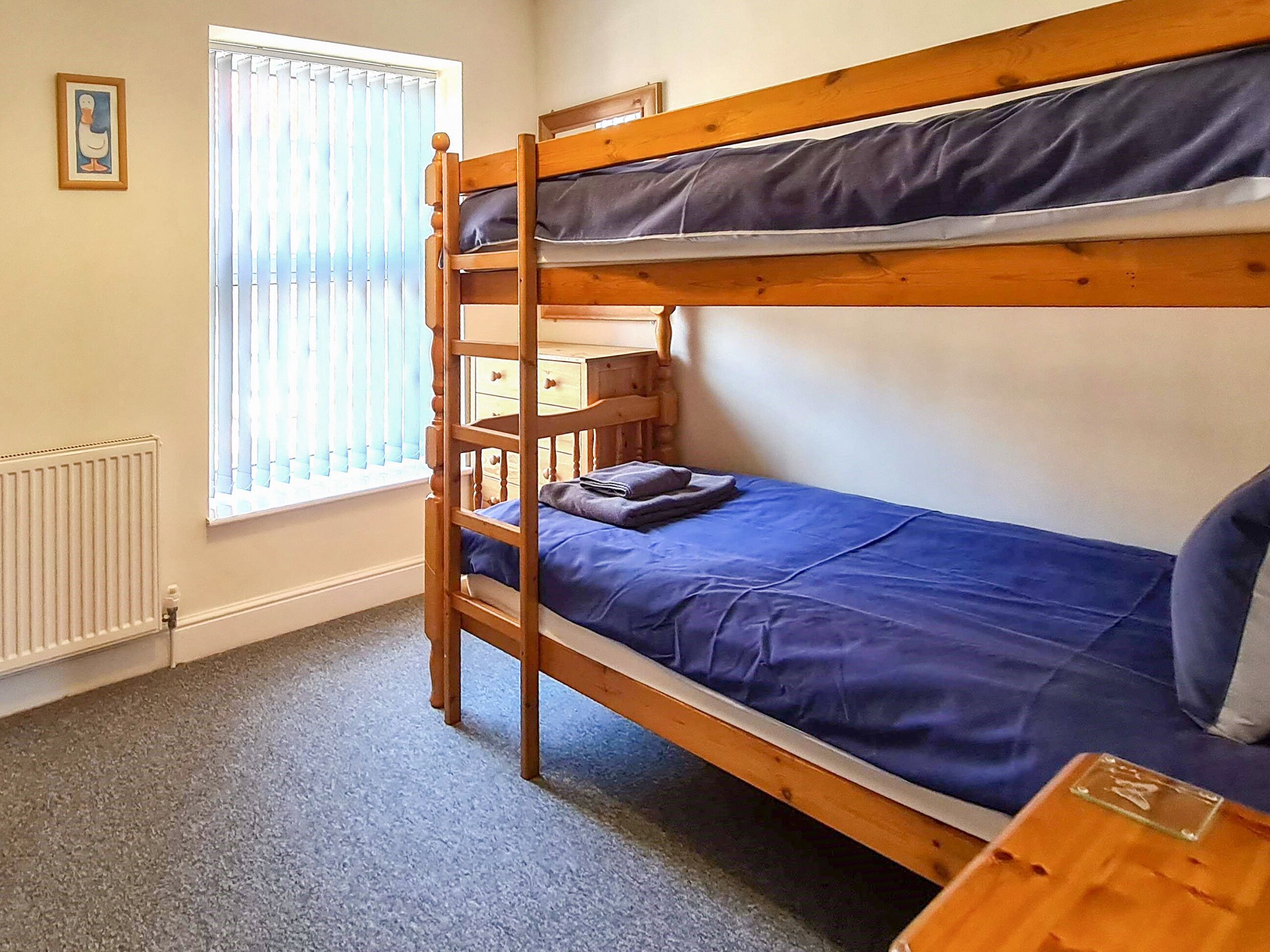 A bunk bed room with a window, a radiator, and a small wooden table.