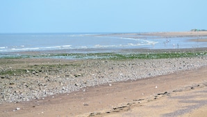 A rocky beach with waves, a clear sky, and distant hills.