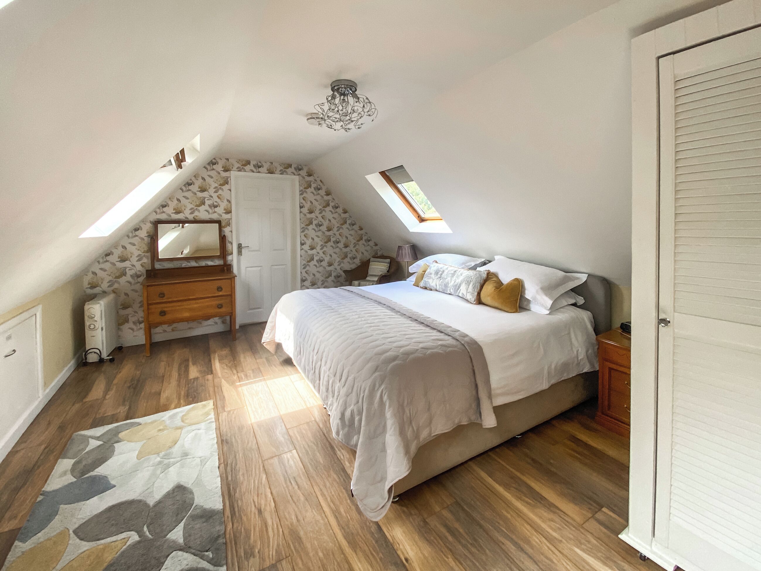 A bedroom with a sloped ceiling, a bed, a dresser, a mirror, a radiator, and a skylight.