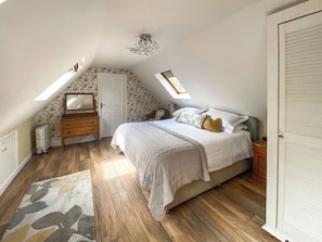 A bedroom with a sloped ceiling, a bed, a dresser, a mirror, a radiator, and a skylight.