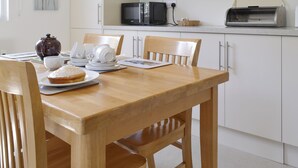 A dining area with a wooden table, chairs, a white cabinet, a microwave, and a toaster. - 2 bedroom accommodation in Scarning, near Dereham (Scarning, near Dereham)
