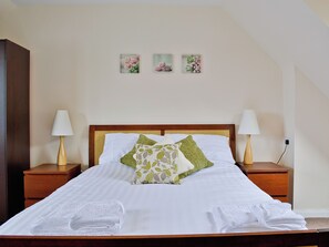Una cama bien hecha con sábanas blancas, dos lámparas de noche y tres cuadros con motivos florales en la pared.