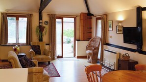 A spacious living room with a high ceiling, wooden beams, a large window, and a television.