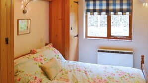 A bedroom with a floral bedspread, a window with plaid curtains, a wall-mounted light fixture, and a radiator.