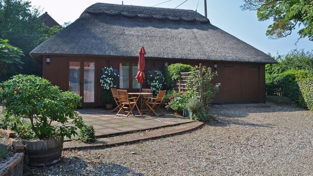 A rustic building with a thatched roof, a wooden porch, and a gravel driveway.
