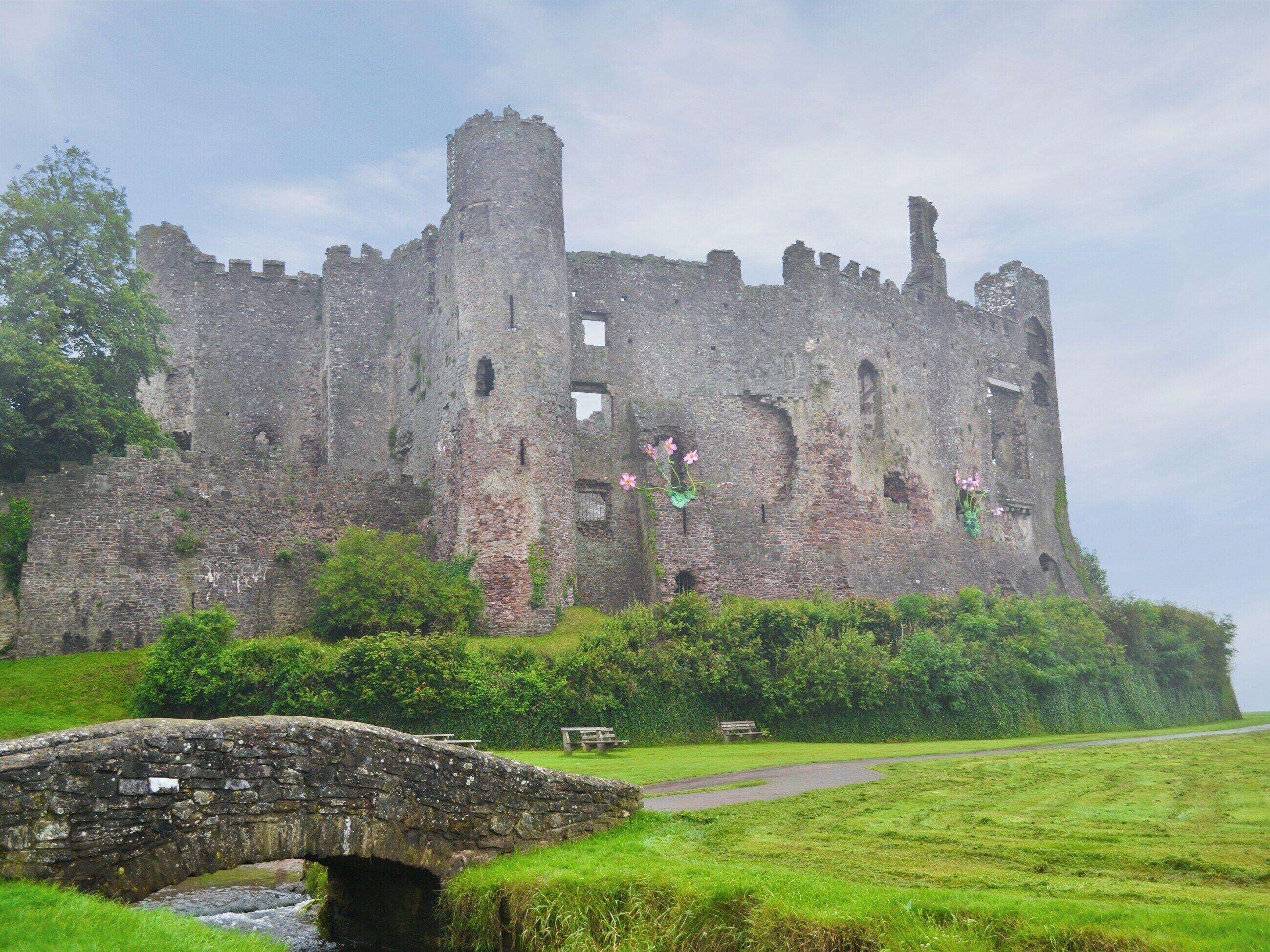 A historic castle with a stone bridge leading to it, surrounded by lush greenery.