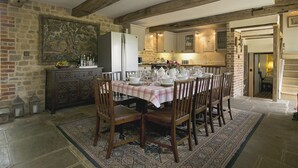 Een eetgedeelte met een grote tafel voor zes personen, omringd door houten stoelen, een kamerkleed met een patroon en een stenen muur.