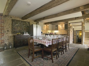 A dining area with a large table set for six, surrounded by wooden chairs, a patterned rug, and a stone wall. - 4 bedroom accommodation in Fernhurst (Fernhurst)