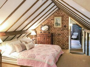 A bedroom with a sloped ceiling, a bed with floral bedding, a wooden dresser, and a mirror.