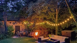 Een achtertuin met vuurkorf, buitenmeubels en lichtjes.