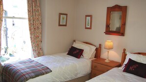 A bedroom with two beds, a nightstand with a lamp, and floral curtains. - A spacious apartment with stunning views of Skiddaw and Latrigg. (Keswick)