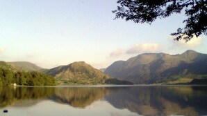A calm lake with mountains in the background and a tree branch in the foreground. - A spacious apartment with stunning views of Skiddaw and Latrigg. (Keswick)