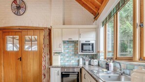 Una cocina con puerta de madera, armarios blancos, microondas, tostadora y un lavamanos.
