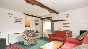 A living room with a floral armchair, a red sofa, a wooden coffee table, and a stone wall. - 3 bedroom accommodation in Gosforth, near Wast Water (Gosforth, near Wast Water)