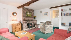 A cozy living room with a brick fireplace, a wooden coffee table, floral-patterned armchairs, and a bookshelf with books. - 3 bedroom accommodation in Gosforth, near Wast Water (Gosforth, near Wast Water)