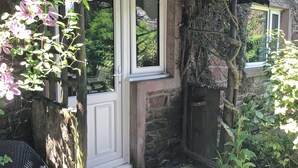A white door with a small window, a brick wall, and a tree with green leaves. - 3 bedroom accommodation in Gosforth, near Wast Water (Gosforth, near Wast Water)