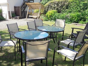 A patio with round glass tables and metal chairs, surrounded by a grassy area and a wooden swing set. - 9 bedroom accommodation in Winterbourne Abbas, near Dorchester (Winterbourne Abbas, near Dorchester)