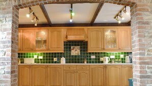 A kitchen with wooden cabinets, a green tiled backsplash, and a brick wall.