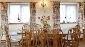 A dining room with a wooden table and chairs, floral curtains, and a vase with flowers.
