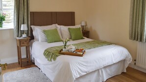Un lit bien fait, avec du linge de lit blanc, des coussins verts, un plateau de petit-déjeuner et une table de chevet avec une lampe.